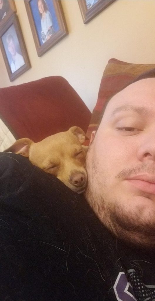a man lying on a couch with a dog sleeping on his shoulder